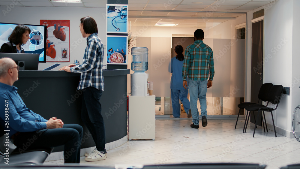 Wall mural Medical assistant asking african american man to attend consultation with doctor after waiting in hospital reception lobby. Waiting room area for healthcare appointment and checkup visit.