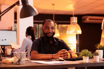 Portrait of african american man working on computer at desk during sunset, using data network. Creating business presentation with research and information to do report in office with big windows.