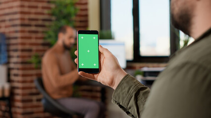 Startup worker using isolated greenscreen on mobile phone, looking at blank mockup display with copyspace background. Analyzing chroma key template on modern smartphone display.