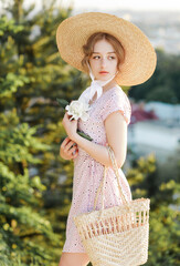Close-up portrait of a tender blonde in a straw hat posing against the background of the city with...