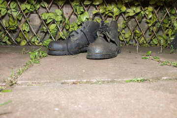 Old garden, black leather boots by a trellis and wall.