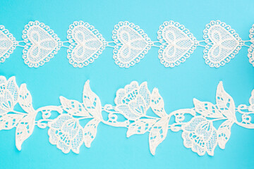 White lace with flowers and leaves, heart shape on blue background horizontally. Close up