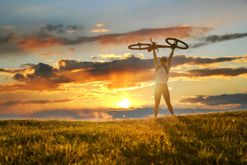 Cyclist celebrating victory holding his bicycle over himself on the sky sunset background. Concept...