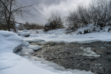 Quiet corner of wild nature on the banks of a narrow river with rapid current in winter. Russia, Ural.