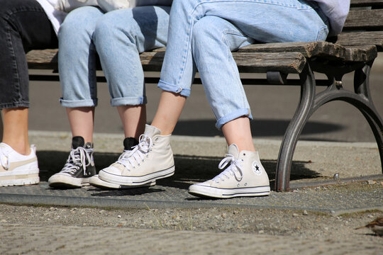 Junge Frauen auf einer Parkbank tragen Chucks. Im Vordergrund helle Chucks, im Hintergrund schwarze Chucks