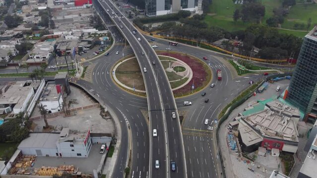 Drone footage of newly built overpass in Lima, Peru above a roundabout called "Ovalo Monitor Huascar" Cars can be seen driving in streets with little traffic on cloudy day. Drone flying forward.