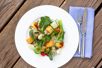 Tasty tuna salad with lettuce, black olives, eggs and fresh vegetables on wooden table