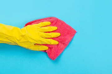 a female hand in a yellow rubber protective glove with a micro fiber red rag wiping a blue wall from dust. A maid or housewife takes care of the house. Spring general or regular cleaning. 