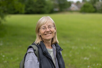 Portrait of smiling middle aged blonde woman wearing glasses standing in the park