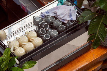 White and black coffee and tee cups on top of a coffee machine in a tropical bar or pub.