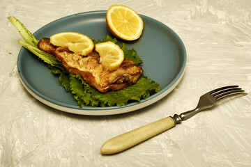 fried fish with lemon and herbs on a plate and a fork on the table