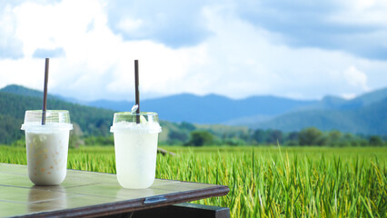 A glass of lemonade and cold fresh milk on a wooden table at a copy space coffee shop. hills and fields nature background