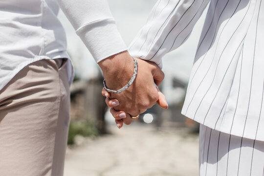 couple holding hands. light image the boy has a bracelet on his hand. the couple is dressed in light and white clothes