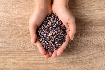 Thai purple rice seed in hand on wooden background, Organic rice grain, Table top view