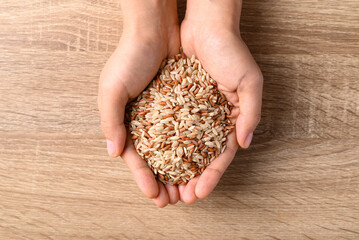 Thai brown rice seed in hand on wooden background, Organic rice grain, Table top view