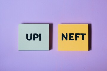 Electronic transferring of fund comparison concept. Sticky note pile with the text UPT and NEFT acronyms on purple background.