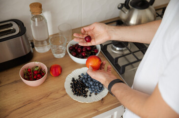 The guy chooses between cherries and nectarine. The guy eats fruit and berries for breakfast. Healthy lifestyle. Summer ration. Cherry, blueberry, currant and nectarine