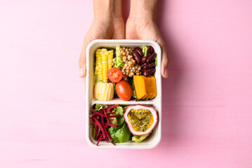 Fresh vegetables salad in biodegradable bowl with hand on pink background, Healthy vegan food