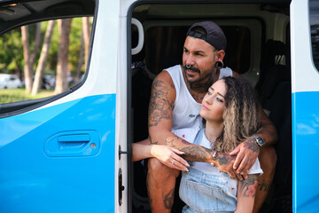 Young tattooed couple hugging and looking at a side, sitting in the side of the van.