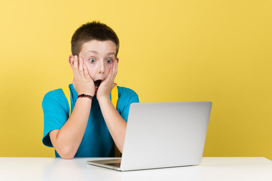 Surprised boy hands on face in front of computer isolated on yellow background. - Powered by Adobe