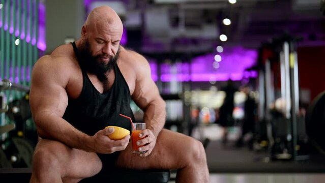 jock is drinking fresh juice in gym, healthy nutrition after training, professional bodybuilder