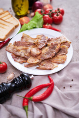 fried bacon pieces in a plate and vegetables at domestic kitchen stone or concrete table