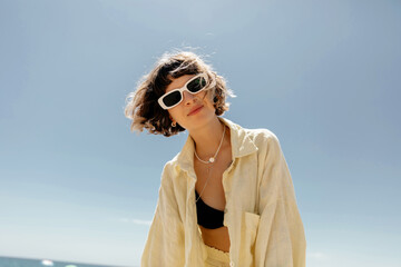Gorgeous young woman posing emotionally with lovely smile against blue sky in sunny day. Pretty...
