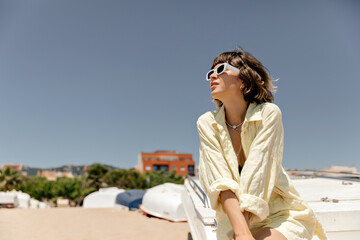 Fashion female model with short hair wearing summer light outfit and white sunglasses posing g...