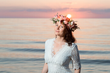 Fototapeta na wymiar Beautiful young woman with a wreath of flowers on her head by the sea at sunset