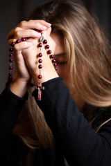 Christianity theme – prayer.  Christian woman with Bible praying with hands crossed keeping rosary.