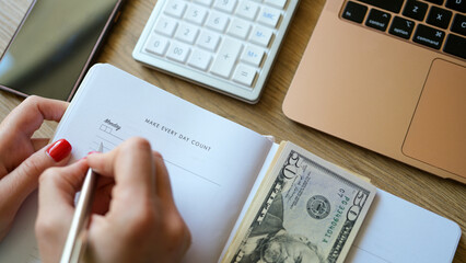 Woman counting money and making notes in notepad