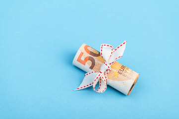 Roll of 50 Euro money with white ribbon isolated on light blue background