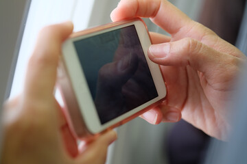 Hands of an Asian woman using a smartphone to take pictures or play games on an airplane.