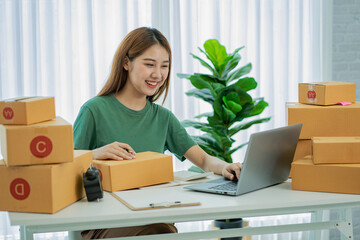 Independent SME Small Business Entrepreneur Portrait of an Asian woman working at home with a laptop taking orders and Online Marketing Packaging Shipping Boxes eCommerce business idea