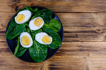 Spinach leaves and halved boiled eggs on a black plate. Top view