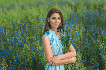 Young pretty woman among the field of beautiful cornflowers closeup