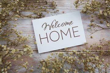 Welcome Home text on paper card with flower decoration on wooden background