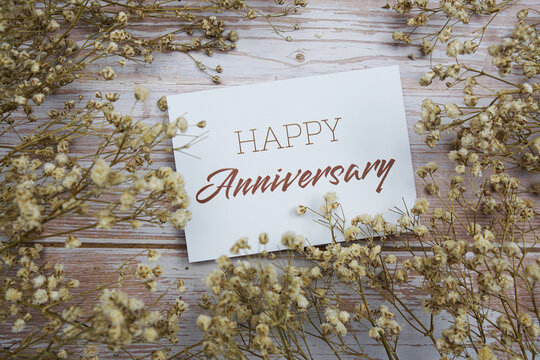 Happy Anniversary text on paper card with flower decoration on wooden background