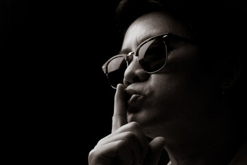 Asian man wearing sunglasses shows a silent gesture with his index finger on his lips black and...