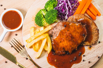 Pork steak with pepper seeds, vegetables and french fries on wooden plate