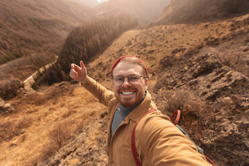 Concept Adventure Traveler with backpack. Hipster man in glasses and red hat takes selfie photo background autumn mountains Altai