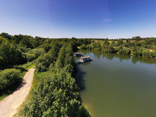 a panoramic view of the green forest and the lake and the glampings standing on the shore on a sunny summer day taken from a drone