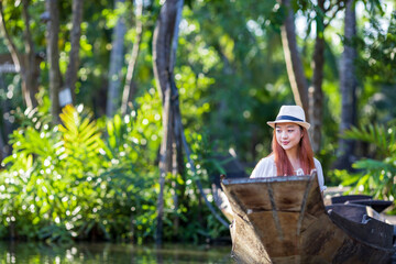 Young Asian woman tourist is travel with wooden boat in floating market in Thailand and having...