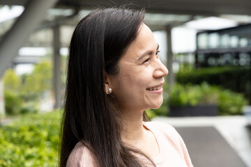 Happy smiling middle aged asian woman in green city environment