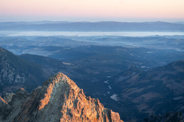 Prominent peak catching sunrise light with mountain range and foggy valley in the background