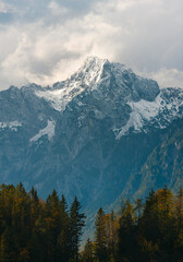 Grintovec mountain at fall. View on mountain peak in Southern Limestone Alps, Slovenia. Alpine peak is lit with day sunlight. Mountain range against clouds, with pine forest on foreground,