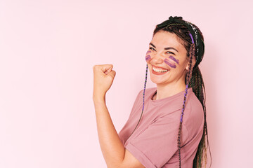 Girl with purple paint on her face clenching her fist against pink background.