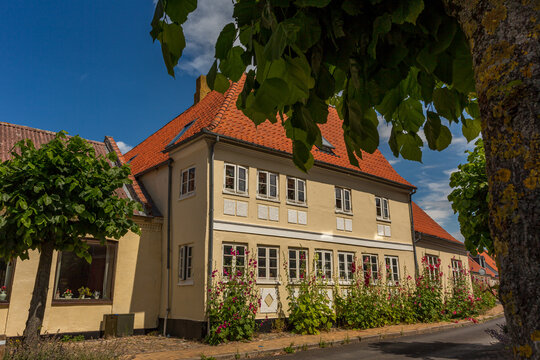 03-07-2022 Assens, Denmark - Old yellow house. Red roof, Blue sky. green trees in the foreground