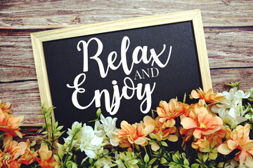 Relax and Enjoy typography text written on wooden blackboard with flower bouquet decorate on wooden background