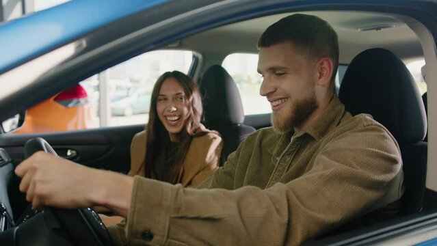A young happy couple looks at each other in a good mood sitting in the cabin of a new car. Buying at a car dealership